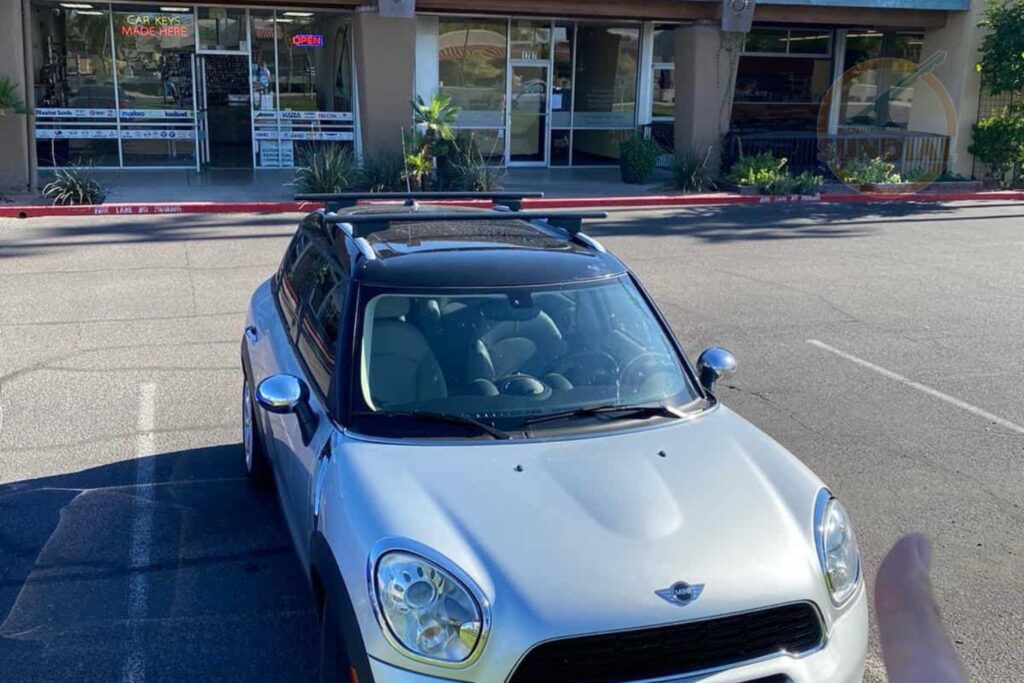 A silver MINI Cooper SUV parked in a sunny parking lot in front of a retail shopping center.