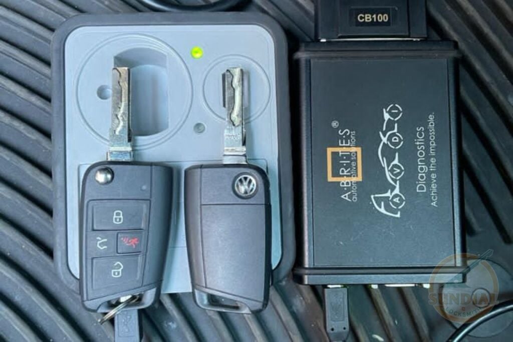 Restricted Keys Explained: How They Stop Unauthorized Copies Two Volkswagen flip key fobs placed next to an All Keys Diagnostics CB100 automotive key programming module on a textured black surface.