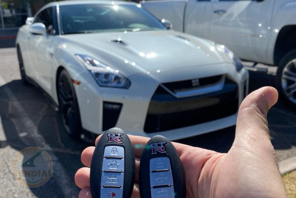 Restricted Keys Explained: How They Stop Unauthorized Copies A hand holding two Nissan GT-R smart key fobs in front of a white Nissan GT-R parked in a lot.
