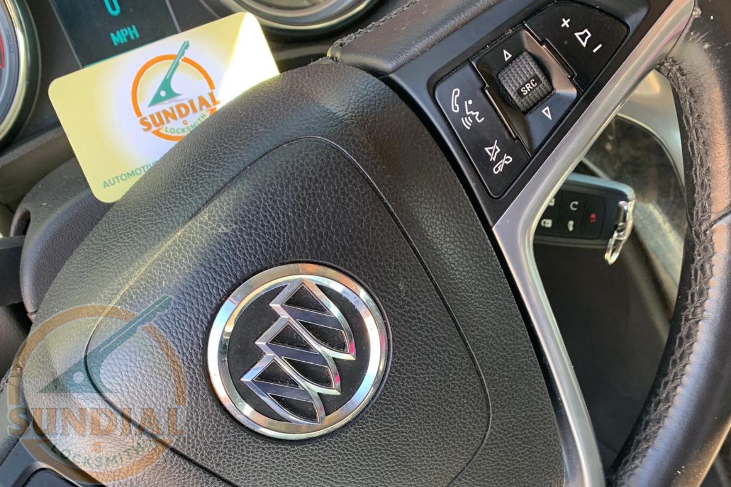 Ignition Replacement: How Much It Costs and How Long It Takes Close-up of a Buick steering wheel with a Sundial Locksmith business card tucked into the dashboard, showing steering column controls.