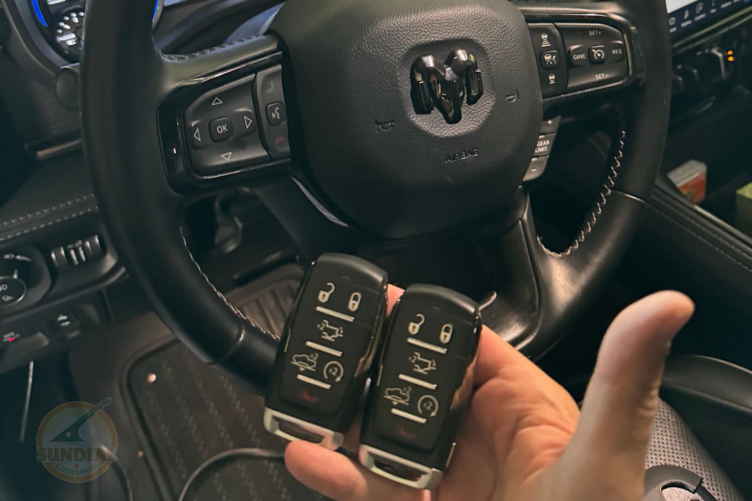 How Long Does 'All Keys Lost' Programming Actually Take? A hand holding two Ram truck smart key fobs in front of a Ram vehicle's steering wheel and dashboard interior.